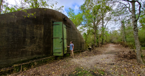 A hiker standing at the entrance of an abandoned WWII storage bunker along a historic hiking trail in Louisiana.
