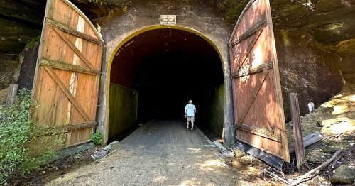 Hiker walking into the Elroy-Sparta State Trail tunnel in Wisconsin, framed by large wooden doors at the entrance.