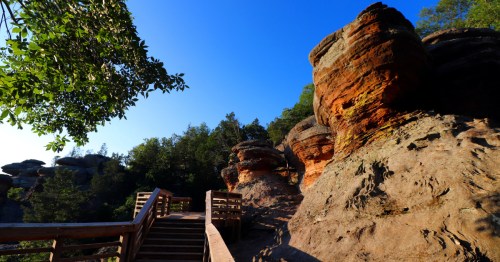 A tan wooden pathway leading up to a viewing platform under a bright blue sky beside reddish rock formations at Garden of the Gods.
