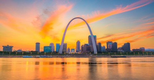 The Gateway Arch dominates the St. Louis skyline and reflects in the Mississippi River at sunset.
