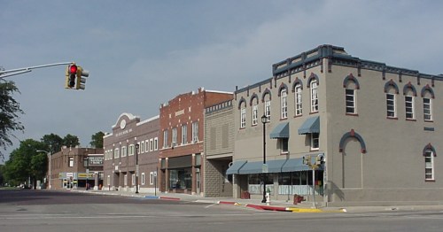 A row of historic downtown buildings, including a prominent light-gray one, at a main street intersection with a stoplight.