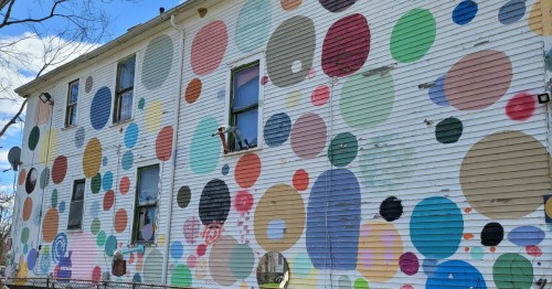 Side of a white, two-story wooden house completely covered in large, multicolored circles and polka dots. 