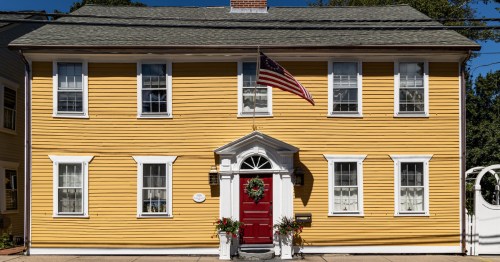 A historic colonial home on the streets of wickford rhode island is painted yellow with a christmas wreath hanging on its red door