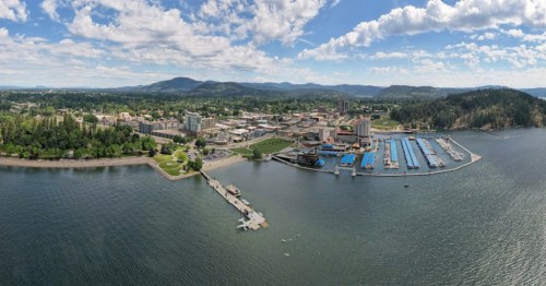 A wide shot of a lakeside town with mountains in the background and clouds overhead.