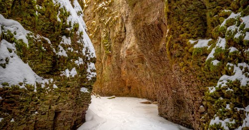 Snow blankets a frozen creek in a narrow slot canyon with rugged rocky walls.