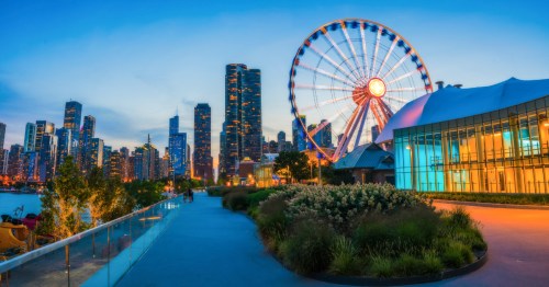 Blue sunset sky behind the skyliine of Chicago. Navy Pier with a brightly lit Centennial Wheel and shopping center are in the foreground.
