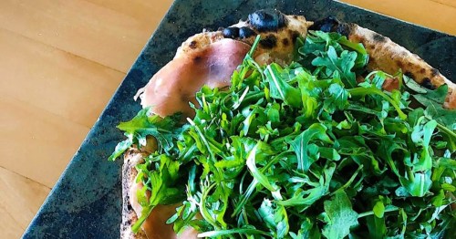 Close-up of a wood-fired pizza, topped with a hefty dose of fresh arugula and prosciutto from Alibi, a popular Wyoming restaurant.