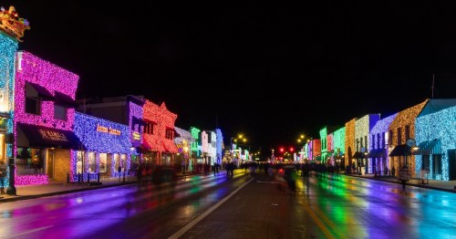 Colorful holiday lights cover the facades of businesses on a dowtwon street at night.