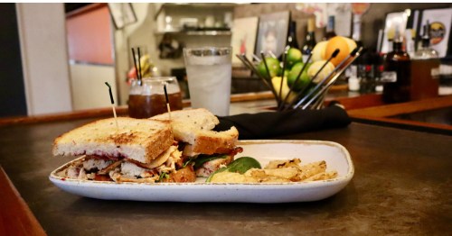 A Sho Nuff sandwich cut in half on toasted bread, served on a white rectangular plate with chips and dip. 