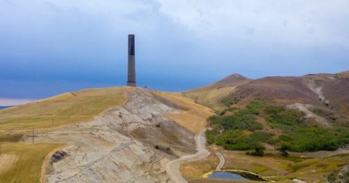 A single smoke stack sits in the distance atop hills of yellowed grass.