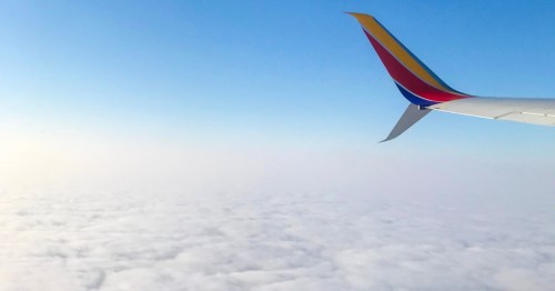 The wingtip of a Southwest Airlines plane flying through the sky above the clouds.