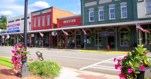 Main Street in Plains, GA, lined with colorful brick storefronts and decorated with American flags and flower plots.