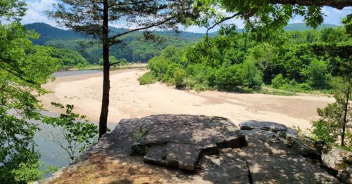 A shaded rock outcropping, overlooking a scenic river in Big Flat, Arkansas, surrounded by rolling hills in the distance.