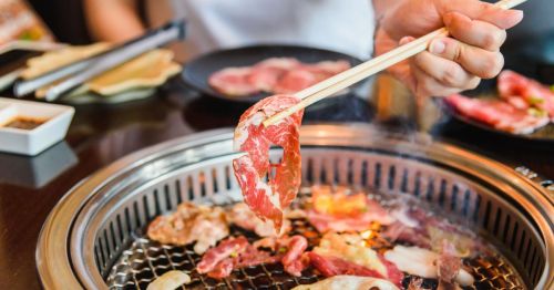 A patron holding chopsticks, cooking a variety of meat at a Japanese-style BBQ restaurant.