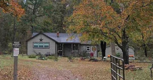 exterior of a small home set behind a fence with a private property sign and trees with changing leaves in fall in jay oklahome