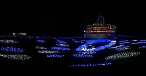 a drydocked ship coverd in christmas lights surrounded by blue lights that look like water at the shelburne museum in Vermont