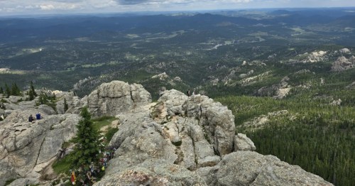 Black Elk Peak, Black Elk Wilderness. A high-angle view from a rocky summit over vast, forested hills and distant mountains.
