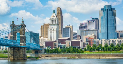 Buildings and a bridge stand along a river with a blue sky.