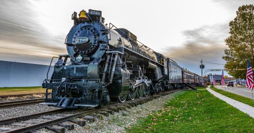 A vintage train stands on tracks with American flags lining a street.