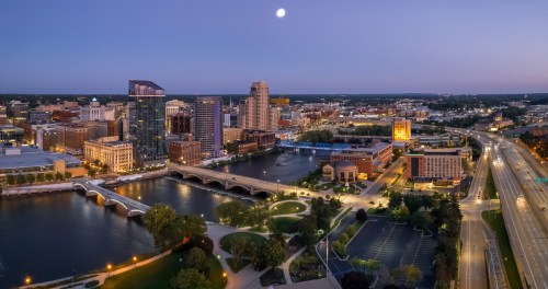Illuminated buildings stand on both sides of a river at twilight.