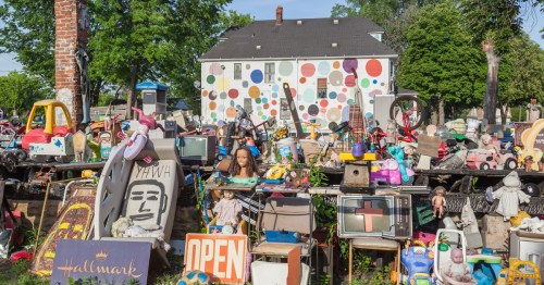 Vintage toys and household items sit outside a white house with colorful polka dots.
