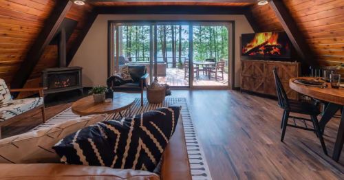 A cabin’s living room with a fireplace, couch, TV, and table.