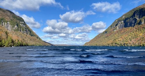 Lake Willoughby's blue waters with waves framed by steep mountains under a partially cloudy sky.