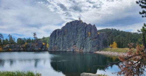 A large rock sticking out from a lake surrounded by forest.