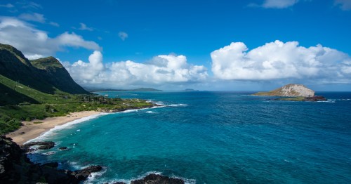 A breathtaking coastal panoramic view showcasing turquoise water, white-sand shoreline, and rugged green cliffs near Makapuʻu Point.