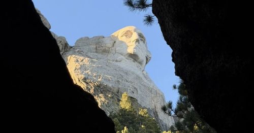 A view of George Washington’s head on Mount Rushmore through a gap between rocks.