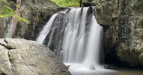 Kilgore Falls cascades over a rock cliff into a clear pool, surrounded by large, smooth boulders.