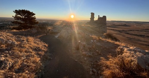 Trail at the Scotts Bluff summit, with the sun rising over the distant plains and rock formations.