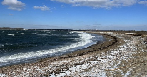 A curved beachfront with snow covering the sand and a frosted wave lapping up on the shore.
