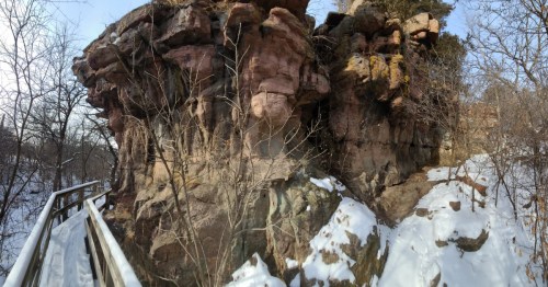 A winter view of Sioux Quartzite cliffs at Palisades State Park. A snowy wooden path is built alongside the sheer rock face.