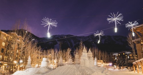 Unique dandelion-shaped holiday lights hang above snow sculptures and pine trees at the base of the ski slopes in Teton Village, Wyoming.