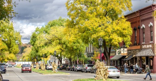 A sunlit, tree-lined street in Wellsboro, PA, featuring the vintage Arcadia Theatre and a classic neon Penn-Wells Hotel sign.
