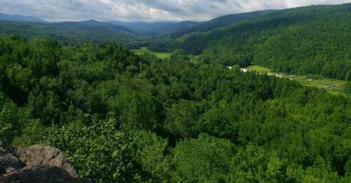 Green mountain vista from the Wu Ledges trail overlooking a deeply forested valley and scattered fields.