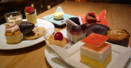 Assorted miniature desserts on plates, including cupcakes, cookies, layered parfaits, chocolate truffles, and mousse cups displayed on a restaurant table.