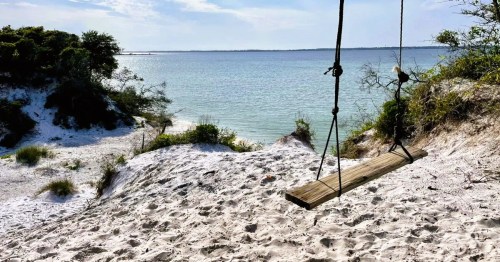 The pristine white sand leads right to the ocean with a swing hanging from a tree overlooking the ocean in Gulf Breeze, FL.