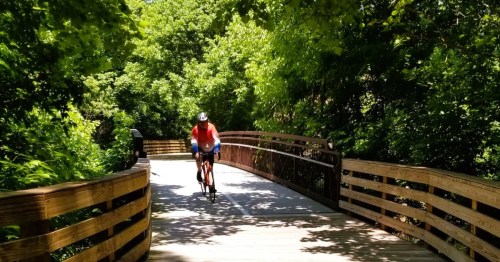 A biker riding along a paved trail leading to a wooden boardwalk in a heavily wooded area in Georgia.