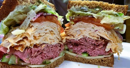 A towering sandwich loaded with turkey, pastrami, lettuce, tomatoes, and cheese, served at a NY-style deli in Atlanta, GA.