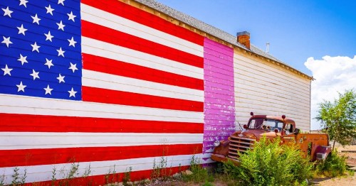 A large American flag painted on the side of a wall with an old vintage truck next to it in Seligman, AZ.