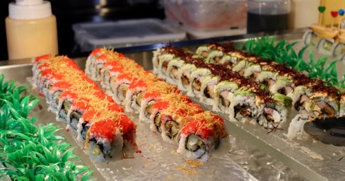 Colorful rows of specialty sushi rolls topped with masago and crunchy tempura flakes on ice.