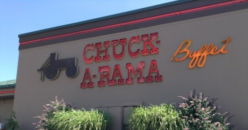 Neon “Chuck-A-Rama Buffet” sign mounted on the exterior of a restaurant building with decorative grasses in the foreground.