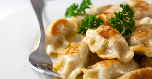 Pan-fried pierogi with golden crispy edges, served on a white plate and garnished with fresh parsley.