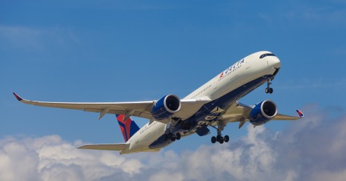 A Delta Air Lines Airbus A350 airplane climbing into a clear blue sky shortly after takeoff, with its landing gear visible and distinctive curved wingtips on display.