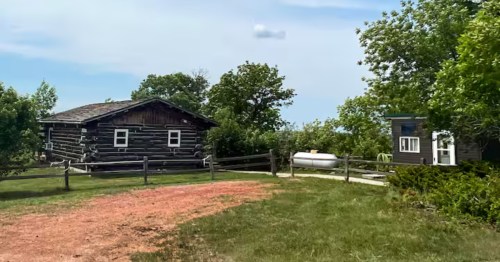  Log cabin rental grounds, showing the main cabin, a detached shed/bunkie, and wooden fencing.