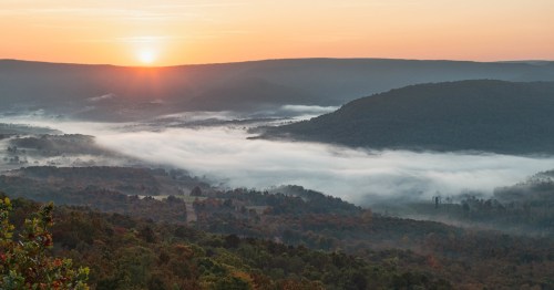Sunrise over layered Ozark Mountains near Jasper, Arkansas, with low-lying fog filling the valley and forested hills fading into the distance.