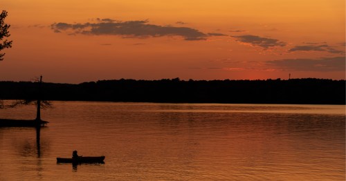 A kayak on Kerr Lake illuminated by a bright orange sunset.