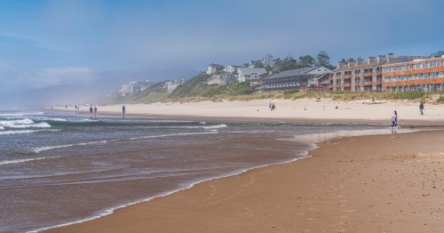 The ocean calmly washes up on the sandy shores of a beachside town on a sunny day.